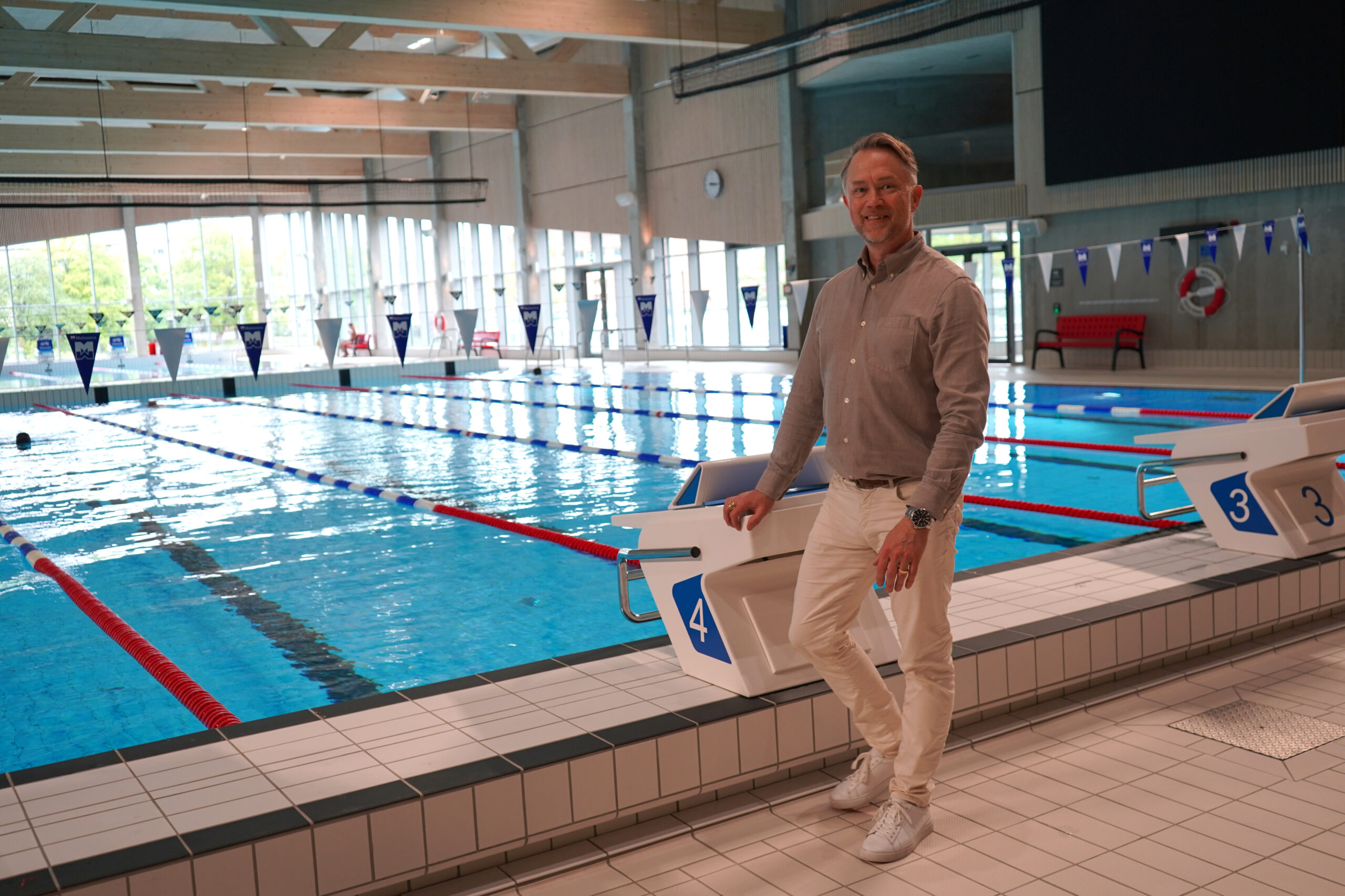 Christian Dahlén står vid 50-metersbassängen och ser glad ut. I bakgrunden ser man stora fönster.